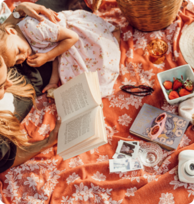 A woman and child laying on the ground reading books.